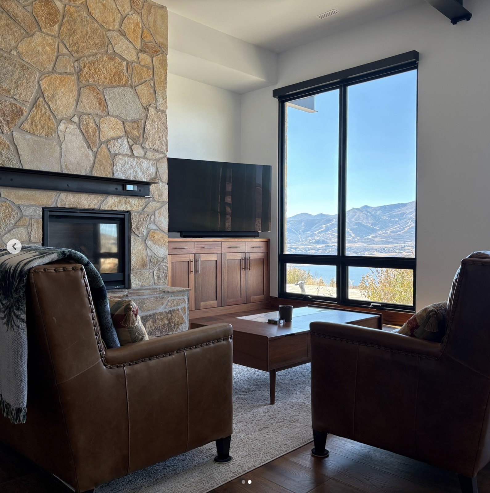 Living room at a Varuna build — full-bed natural stone fireplace beside a floor-to-ceiling window opening to the Wasatch.
