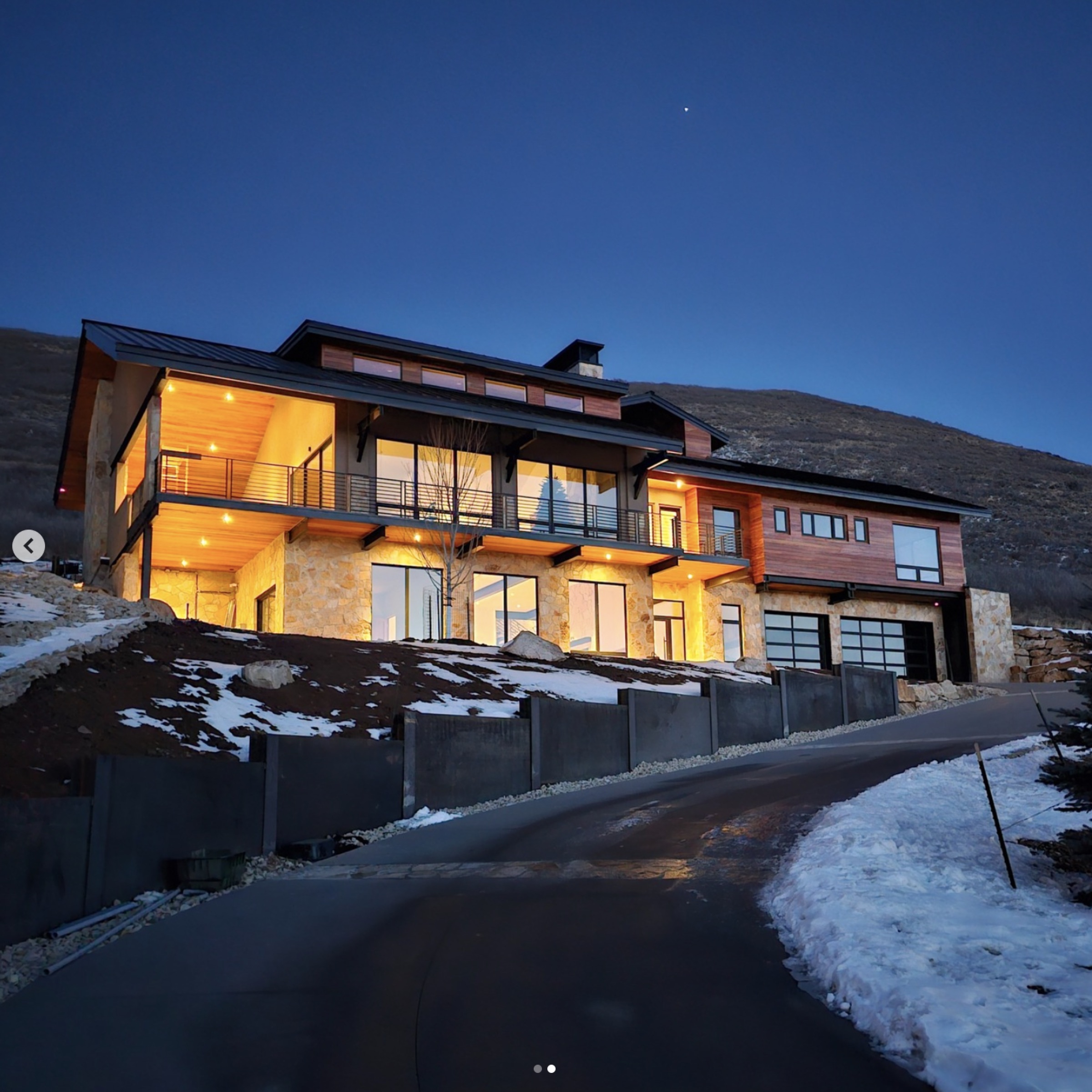 Varuna's signature mountain modern residence at twilight — interior glow against a deep evening sky on a snowy Wasatch hillside.