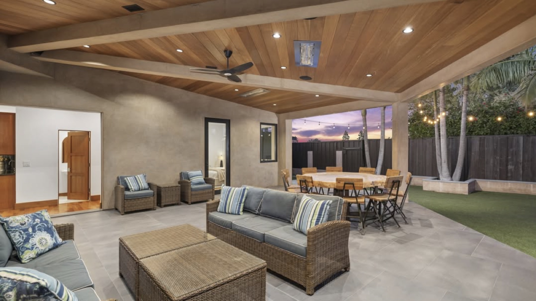 Indoor-outdoor patio at a Varuna build, lit warm under a wood-clad ceiling at dusk.